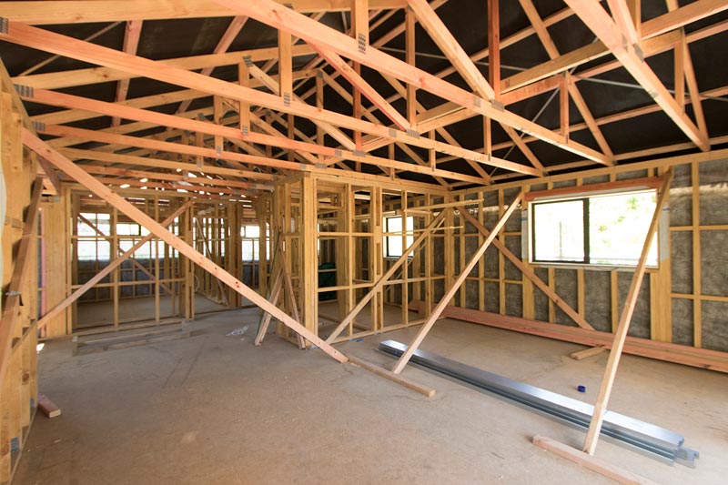 New home under construction with exposed timber framing and roof trusses, symbolising the building process.